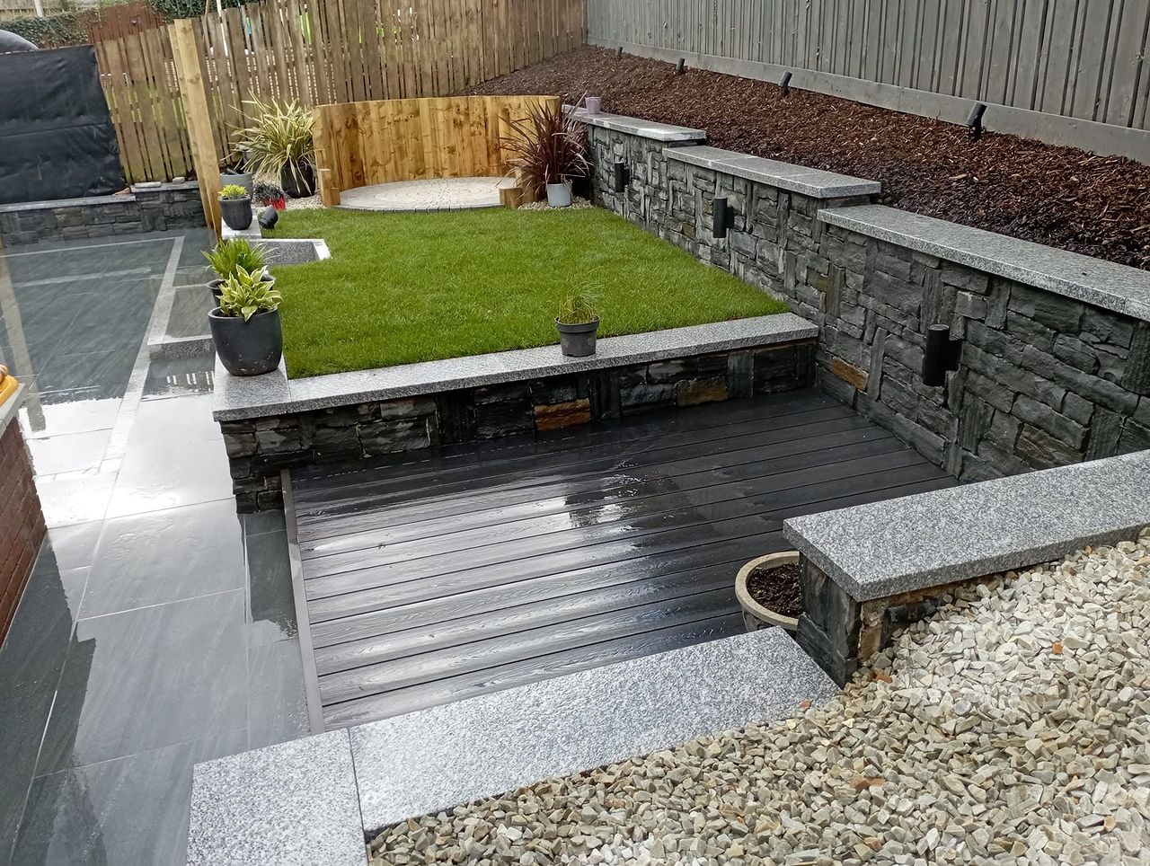 Contemporary garden built by S & H Garden Solutions with stone-clad raised beds, artificial lawn and composite decking