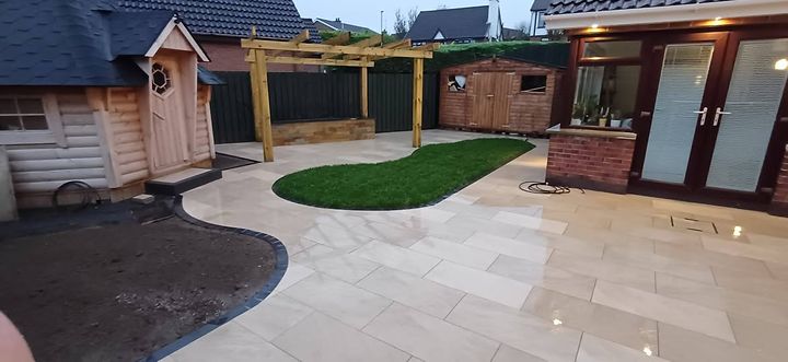 Wide view of a finished garden with pergola, porcelain paving and a curved artificial lawn