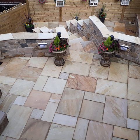 Indian sandstone patio with curved stone-clad seating walls, recessed wall lights and planted urns