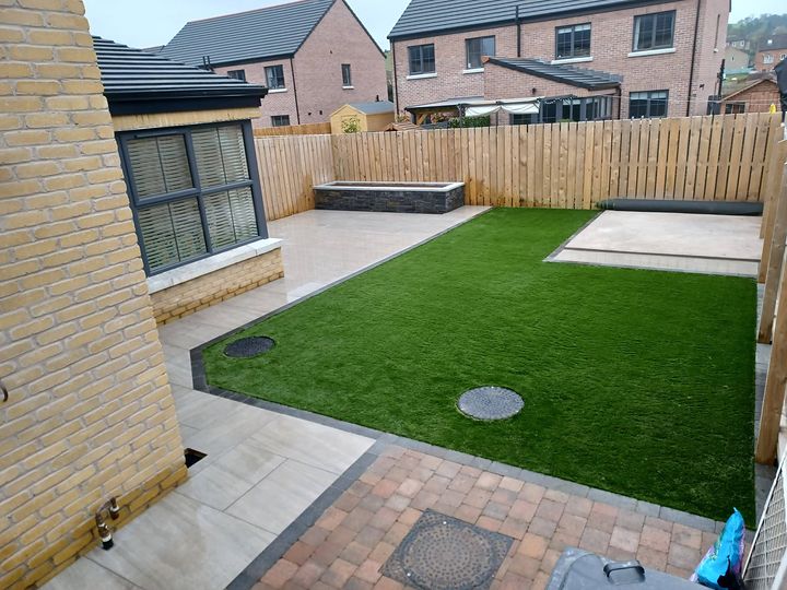 A finished garden with porcelain paving, artificial lawn and a stone-clad raised planter